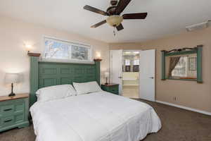Bedroom with dark carpet, ensuite bath, and ceiling fan