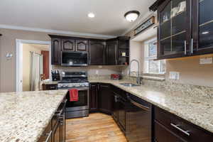 Kitchen with stainless steel appliances, dark wood finish cabinetry, light stone countertops, light wood-type flooring, and ornamental molding