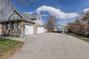 View of side of property featuring driveway, brick siding, and roof with shingles