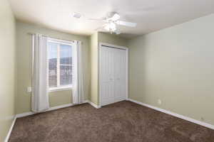 Unfurnished bedroom with dark carpet, a closet, and ceiling fan