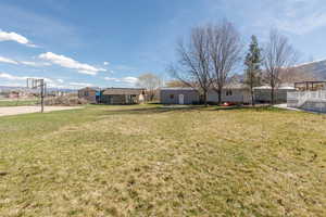 View of grassy yard with a mountain view and basketball court