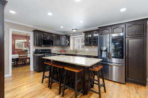 Kitchen with stainless steel appliances, a breakfast bar area, dark wood finish cabinetry, glass insert cabinets, and light wood-type flooring
