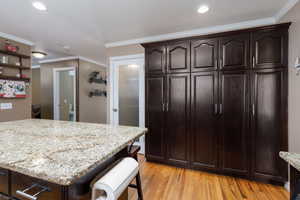 Kitchen featuring dark wood finish cabinets, a kitchen breakfast bar, ornamental molding, light stone counters, and light wood-type flooring