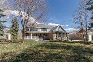 Back of house featuring covered porch, a lawn, brick siding, and a shed