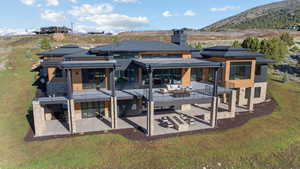 Rear view of house with stone siding, a patio area, a yard, and a mountain view
