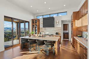Two tone kitchen with a kitchen breakfast bar, light stone countertops, an island with sink, a mountain view, and dark wood finished floors