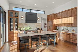Kitchen with decorative backsplash, light wood-type flooring, recessed lighting, a kitchen breakfast bar, and a center island with sink