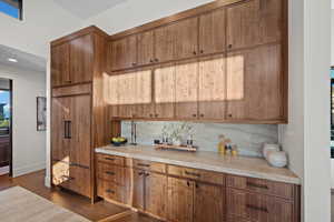 Kitchen with paneled built in refrigerator, light countertops, wood finish cabinets, tasteful backsplash, and dark wood-style flooring
