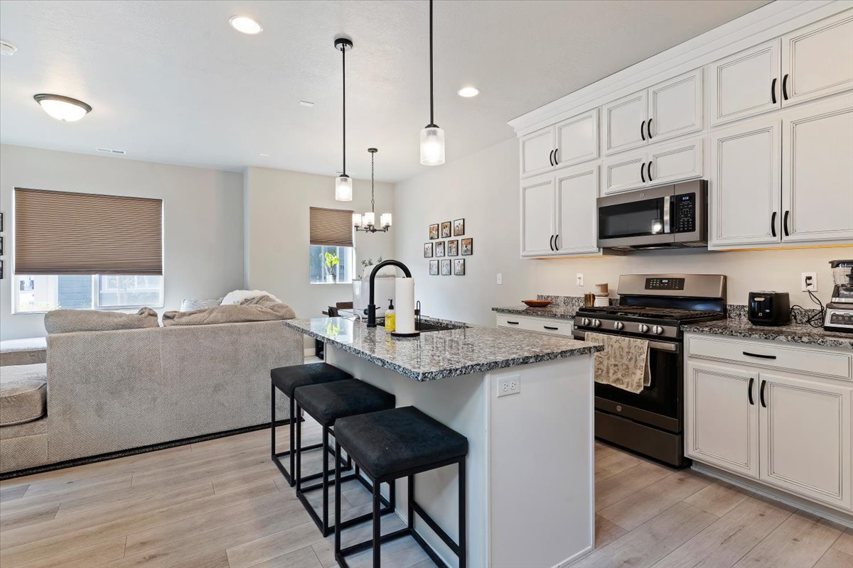 Kitchen featuring stainless steel appliances, a breakfast bar, light stone counters, a center island with sink, and light wood-style floors