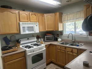 Kitchen featuring white appliances, light countertops, light tile patterned floors, and wood finish cabinets
