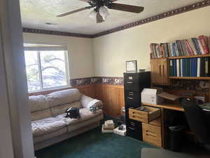 Office space with a wainscoted wall, a ceiling fan, carpet, wood walls, and a textured ceiling