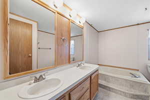 Bathroom featuring double sinks, extended vanity space, and a soaking tub with tile surround.