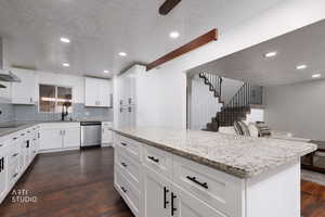 Kitchen featuring light stone countertops, white cabinetry, stainless steel dishwasher, recessed lighting, and a textured ceiling