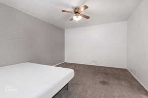 Bedroom featuring brick wall, dark colored carpet, and a ceiling fan