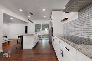Kitchen featuring a breakfast bar area, light stone countertops, black electric stovetop, dark wood finished floors, and white cabinets