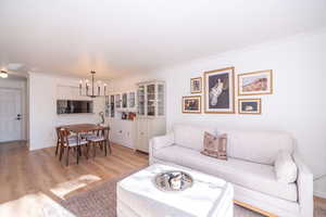 Living area with light wood-style flooring, crown molding, and hanging lights