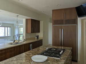 Kitchen featuring paneled built in fridge, stainless steel gas stovetop, light stone countertops, light wood finished floors, and a center island