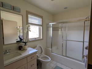 Full ensuite bathroom featuring vanity, shower / bath combination with glass door, and light tile patterned flooring