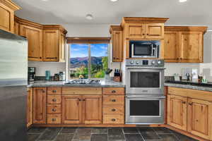 Kitchen with stainless steel appliances, dark stone finish flooring, a mountain view, wood finish cabinetry, and recessed lighting