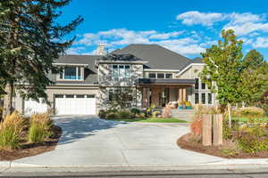 View of front facade with covered porch, driveway, a shingled roof, an attached garage, and a chimney
