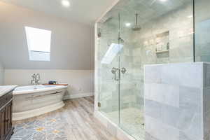 Primary full bathroom featuring a skylight, a stall shower, vanity, a freestanding bath, and light wood-type flooring