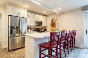 Kitchen with stainless steel appliances, a kitchen bar, white cabinetry, light wood-type flooring, and recessed lighting