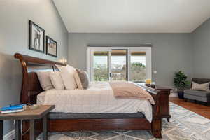 Primary bedroom with wood finished floors, vaulted ceiling, and access to exterior