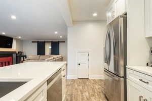 Kitchen with stainless steel appliances, white cabinetry, a barn door, light stone counters, and recessed lighting