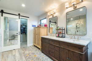Primary full bathroom with double vanity, a shower stall, a spacious closet, light wood finished floors, and recessed lighting