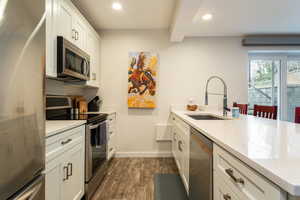 Kitchen with stainless steel appliances, a peninsula, white cabinets, light stone countertops, and dark wood finished floors