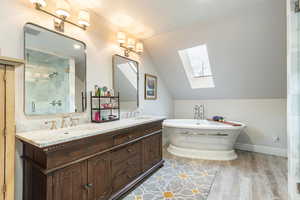 Primary full bathroom with a skylight, double vanity, vaulted ceiling, light wood finished floors, and a freestanding bath
