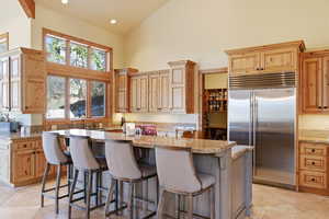 Kitchen with stainless steel built in refrigerator, lofted ceiling, a kitchen bar, recessed lighting, and a kitchen island with sink