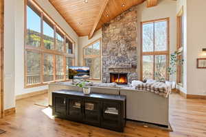 Living room with a fireplace, a high wood beamed ceiling, light wood-style floors, and plenty of natural light