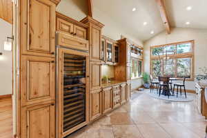Kitchen with beverage cooler, glass fronted cabinets, vaulted ceiling, light stone counters, and a chandelier