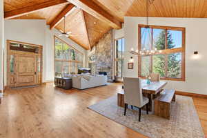 Dining room with a chandelier, light wood-style flooring, a high wooden beamed ceiling, a fireplace, and ceiling fan