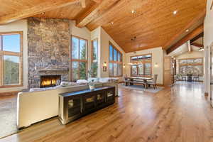 Living room featuring light wood finished floors, a fireplace, a high wood beamed ceiling, and hanging lights