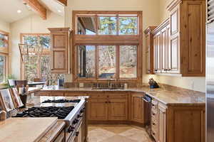 Kitchen featuring wood finish cabinets, stainless steel appliances, suspended lighting, lofted ceiling, and light stone countertops