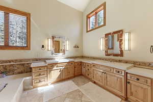 Full bath with double vanity, vaulted ceiling, and light tile patterned flooring