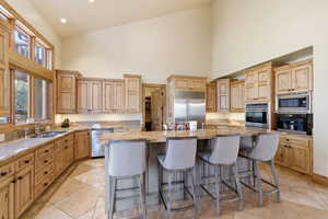 Kitchen with a breakfast bar, built in appliances, a high ceiling, a center island, and recessed lighting