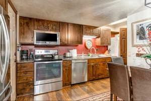 Kitchen featuring stainless steel appliances, a textured ceiling, dark wood-style floors, dark stone countertops, and wood finish cabinets