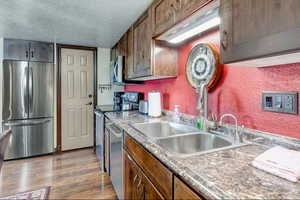 Kitchen with stainless steel appliances, a textured ceiling, light wood-style flooring, and wood finish cabinetry