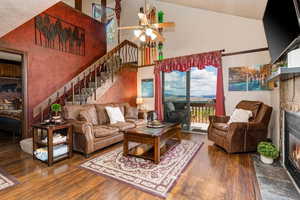 Living room with a tiled fireplace, dark wood-style floors, a ceiling fan, and lofted ceiling