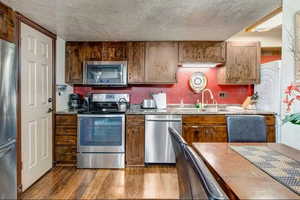 Kitchen with stainless steel appliances, a textured ceiling, dark stone countertops, and light wood-style flooring