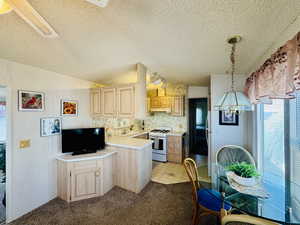 Kitchen with light wood finish cabinets, light countertops, white range with gas cooktop, wallpapered walls, and a textured ceiling
