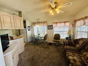 Living area featuring a textured ceiling, a ceiling fan, and dark carpet