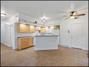 Kitchen with light wood finish cabinets, light countertops, ceiling fan, white appliances, and a kitchen island