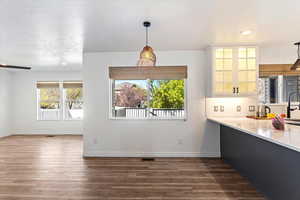 Kitchen with decorative light fixtures, dark wood-style floors, backsplash, glass insert cabinets, and light stone counters