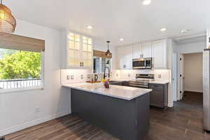 Two tone kitchen with two tone color scheme, pendant lighting, a peninsula, stainless steel appliances, and dark wood finished floors