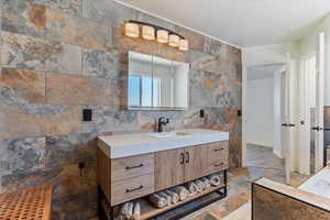 Bathroom with vanity, tile walls, stone tile floors, and a garden tub
