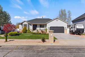 Ranch-style house with covered porch, driveway, an attached garage, a front yard, and roof with shingles